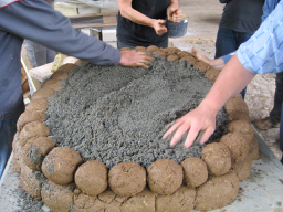 Lehmofenbau ist Teamwork. Hier wird das Fundament erstellt. Auf den Sand kommen später die Schamottsteine.